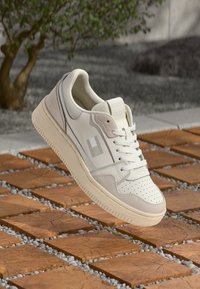 White sneaker featuring a smooth leather upper, perforated toe, and light suede accents. Soft sole, minimalistic design, and subtle branding.