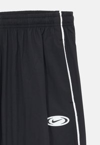 Čierne športové šortky s elastickým pásom, bielym bočným prúžkom a bielym oválnym logom Nike blízko lemu.