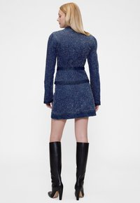 Džinsinė striukė su pritaikyta forma, tekstūruota mėlyna medžiaga ir atitinkama mini sijonu, derinama su juodais aukštakulniais batais iki kelių.