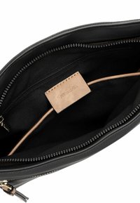 Interno di una borsa in pelle nera con una texture liscia, tasca con zip e un'etichetta beige con il marchio. Fodera in tessuto nero.