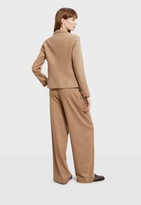 Bež vuneni sako s prilagođenim krojem, visokim ovratnikom i dugim rukavima, uparen s hlačama širokih nogavica, oba s mekom teksturom.