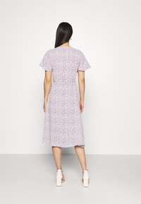 Violetti kukallinen mekko, jossa on lyhyet liehuvat hihat, istuva vyötärö ja virtaava polvipituinen helma. Yhdistetty valkoisiin paksupohjaisiin kenkiin.