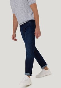 Donkerblauwe denim jeans met opgerolde boorden, gecombineerd met een lichtgrijze shirt met korte mouwen en structuur, en witte sneakers. Eenvoudig ontwerp, casual pasvorm.