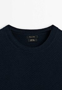 Pull en laine texturée bleu marine foncé avec col rond et étiquette de marque cousue à l'intérieur du col.