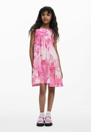 Ružové kvetinové šaty s rozšíreným strihom, okrúhlym výstrihom a nazbieraným pásom. Kombinované s ružovými sandálmi a bielymi volánovými ponožkami.