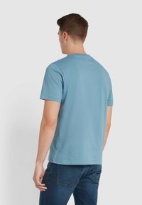 T-shirt a maniche corte, girocollo, in cotone azzurro chiaro, con una superficie liscia e un design semplice, indossato con jeans blu scuro.