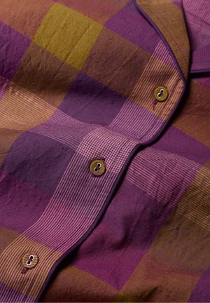 Chemise à carreaux dans des nuances de violet et d'or, avec un tissu texturé, un design à boutons, et deux boutons ronds avec des coutures contrastantes.
