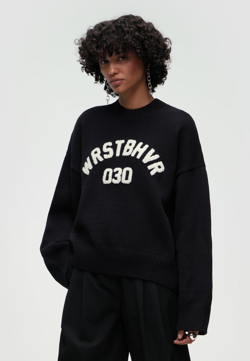 Czarny sweter z dzianiny z białym napisem "WRSTBHV 030." Oversized krój, dekolt typu crew neck oraz ściągacze na rękawach i u dołu. Teksturowany materiał.