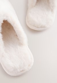 Chaussons blancs duveteux avec une texture douce et pelucheuse ; design arrondi ; ouverture à l'arrière ; semelle épaisse et rembourrée. Convient pour une utilisation en intérieur.
