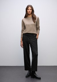 Beige stickad tröja med långa ärmar, i kombination med svarta rutiga byxor och svarta ankelboots. Enkelt design, mjuk textur, avslappnad passform.