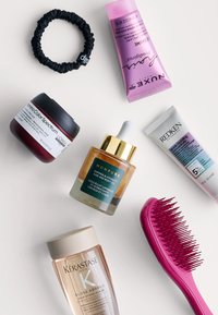 Samling av hår- och hudvårdsprodukter: en glänsande röd burk, en guld dropperflaska, en rosa tub, en klar squeeze-tub och en rosa hårborste.