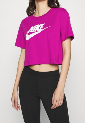Kvinde iført en lyserød cropped Nike T-shirt og sorte leggings med høj talje, stående foran en ensfarvet hvid baggrund.