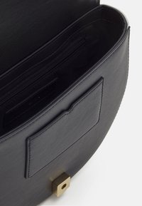 Svart läderhandväska med slät yta, innerficka med dragkedja, yttre ficka utan stängning och en gyllene fyrkantig detalj i basen.