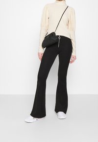 Beige ribbattu with puff-sleeved turtleneck, yhdistetty mustiin ribballisiin farkkuihin. Mukana musta crossbody-laukku ja valkoiset lenkkarit.