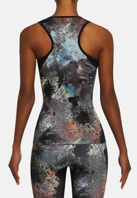 Kobieta w bezrękawniku sportowym z wycięciem na plecach oraz dopasowanych legginsach w abstrakcyjny, wielokolorowy wzór z plamami i ostrymi liniami.