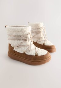 Bottines marron à la cheville avec une tige en polaire blanche et duveteuse, dotées de lacets décoratifs et de ferrures dorées. Semelles épaisses en caoutchouc pour une bonne adhérence.