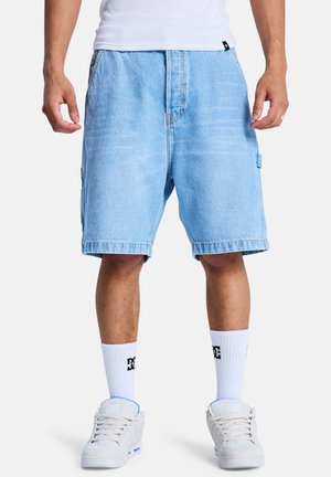 Hellblaue Jeansshorts mit lockerem Schnitt, mit abgesteppten Nähten, umgeschlagenen Säumen und Seitentaschen. Kombiniert mit weißen Socken und hellen Schuhen.