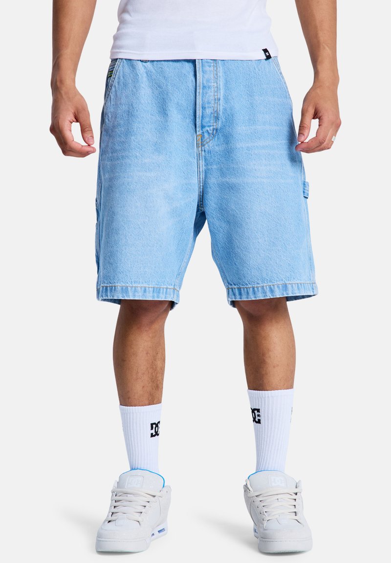 Lichtblauwe denim shorts met een relaxte pasvorm, voorzien van gestikte naden, omgeslagen zomen en zijzakken. Gecombineerd met witte sokken en lichte schoenen.
