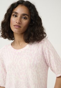 Pull à manches courtes en tricot doux, rose clair avec un motif léopard subtil en blanc. Présente un col rond standard et une coupe décontractée.