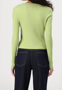 Rippstrick-Langarmoberteil in Hellgrün mit figurnahen Schnitt und rundem Ausschnitt, kombiniert mit dunkelblauen High-Waist-Jeans.