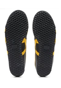 Svarta och gula sportskor med en texturerad gummiyttersula, som har ett distinkt triangulärt mönster och sidokutningar för ventilation.