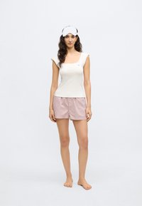 Jasno kolorowy bawełniany tank top z krótkimi rękawami, w parze z różowo-białymi szortami w paski. Na głowie znajduje się biała opaska na oczy do spania.