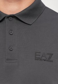 Gray polo shirt made of cotton blend, featuring a collar, three button placket, and an embossed EA7 logo on the left chest.