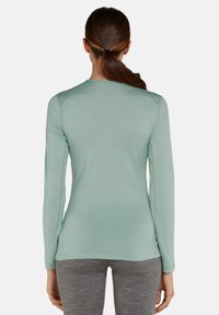 Top a maniche lunghe di colore verde menta realizzato in tessuto leggero, caratterizzato da un colletto tondo e un design slim fit, abbinato a pantaloni grigi attillati.