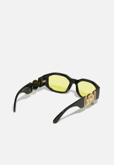 Óculos de sol pretos com lentes amarelas; design de armação octagonal; detalhe em tom dourado na haste; textura brilhante.