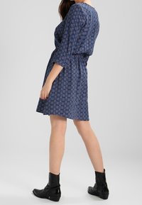 Robe à motifs bleus avec des manches trois-quarts, taille cintrée et jupe évasée. Portez-la avec des bottines noires.