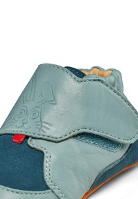 Zapato infantil azul-verde, fabricado con materiales de cuero y ante, que presenta un diseño de conejo, acentos rojos y una correa de velcro ajustable.