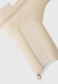 Beige ankelstøvel laget av teksturert lær med en kraftig såle, utstyrt med et logomerke og elastiske sideakenter.