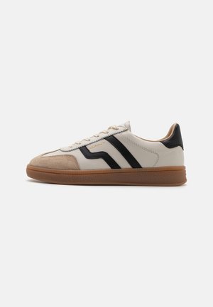 Weiße Sneaker mit schwarzen Streifen und einer Wildleder-Zehenkappe. Verfügt über eine strukturierte Gummisohle und beige Akzente. Schnürsenkel im klassischen Stil.