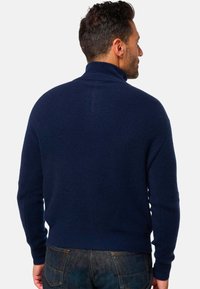 Pull en laine côtelée bleu marine, confectionné dans un tissu doux, avec des manches longues et une taille cintrée, vu de dos.