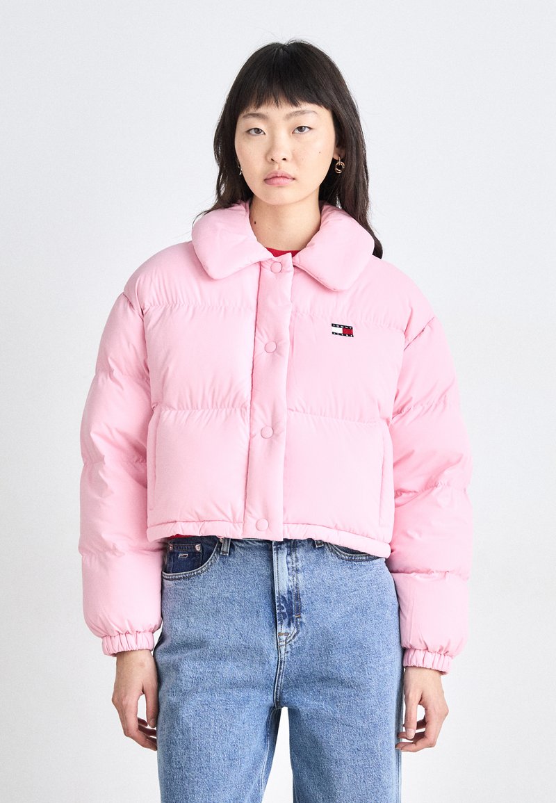 Rosa kort puffjacka med krage, knappstängning och elastiska ärmslut. Buren över blå jeans med en liten logopatch.