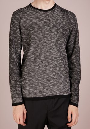 Pull en tricot texturé noir et blanc avec un col rond et des manches longues, présentant une bordure contrastante noire au niveau du col et de l'ourlet.
