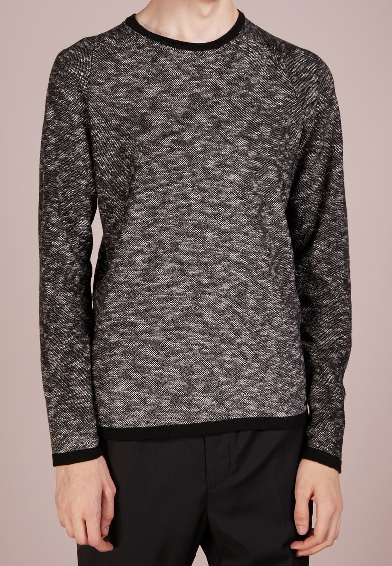Pull en tricot texturé noir et blanc avec un col rond et des manches longues, présentant une bordure contrastante noire au niveau du col et de l'ourlet.