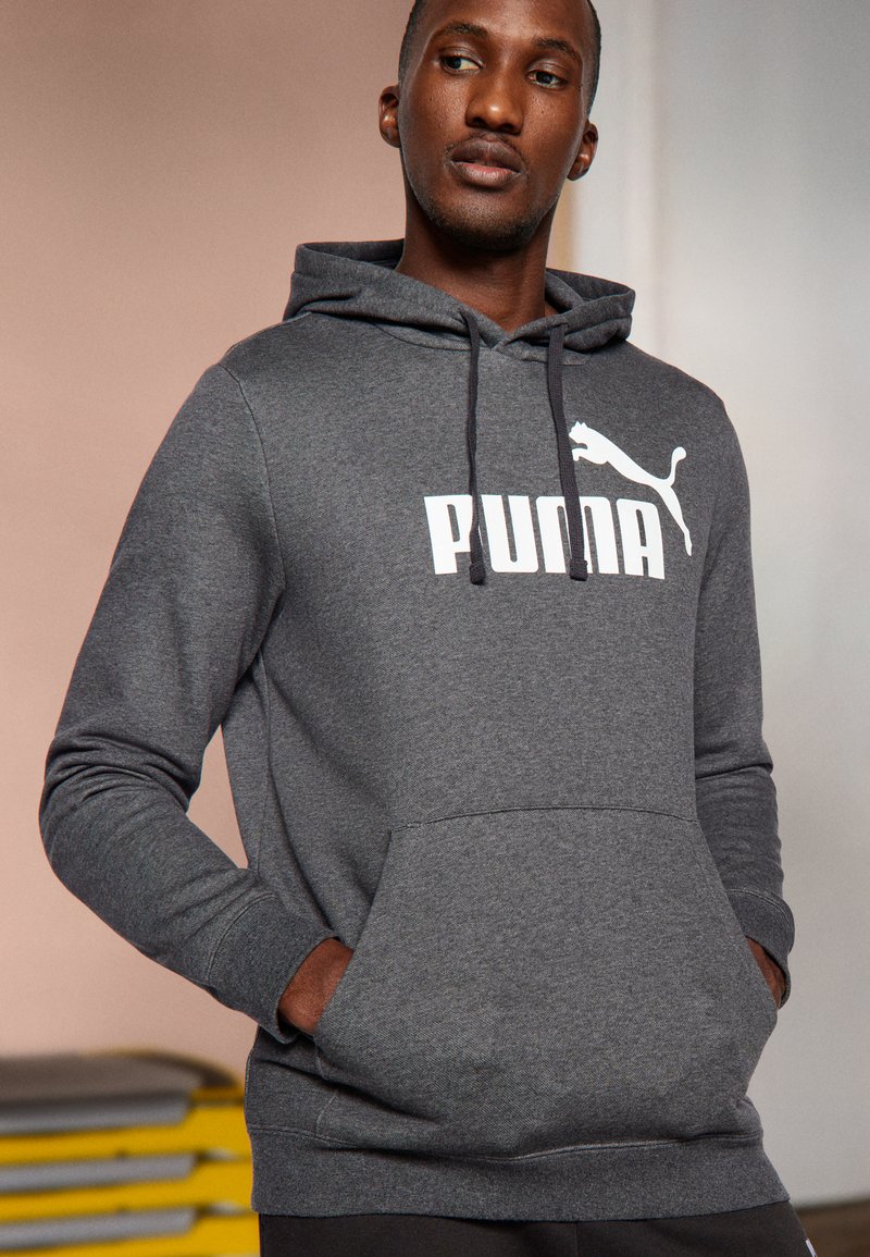 Sudadera gris hecha de una tela suave, con un gran logo blanco de "PUMA", bolsillo tipo canguro y capucha ajustable con cordones.