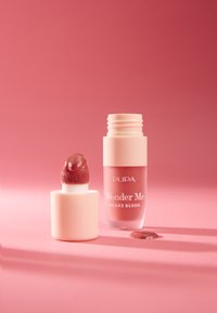 Colorete líquido en un bote transparente rosa con una punta aplicadora suave. El producto es de un tono rosado apagado, colocado sobre un fondo rosa.