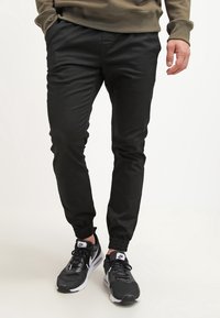 Pantalons de jogging noirs avec des poignets élastiques et des poches avant, assortis à des baskets Nike noires avec un logo blanc et des semelles amortissantes.