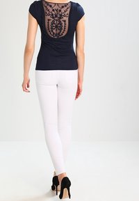 Námořnické tričko s krajkovými detaily na zádech, krátké rukávy, kombinované s bílými úzkými džíny a černými lodičkami. Pohled z kufru.