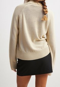 Beżowy sweter dzianinowy z ribbowym wykończeniem u dołu i na mankietach, z wysokim kołnierzem. Połączony z dopasowaną czarną spódnicą.