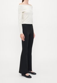 Top blanco de canalé sin mangas combinado con pantalones negros acampanados y zapatos planos negros. Diseño simple, texturas suaves y silueta ajustada.