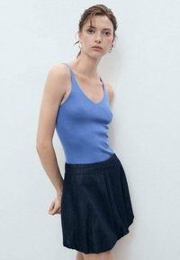 Light blue ribbed tank top with narrow straps paired with a dark denim pleated skirt. Simple design, smooth texture, and clean lines.