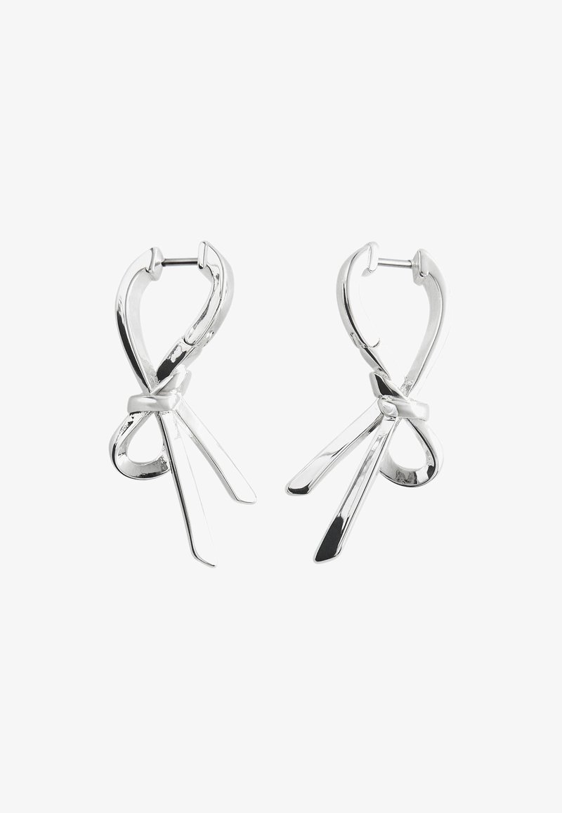 Silberne Creolen mit einem gedrehten Design, die zwei längliche, spitz zulaufende Akzente aufweisen, die an Bänder oder Scheren erinnern. Polierte Oberfläche.