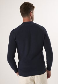 Marineblaues Rippstrick-Pullover mit rundem Kragen, langen Ärmeln und schmalem Saum. Der Stoff wirkt weich und strukturiert, ideal für die Freizeit.