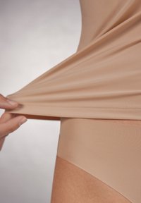 Beige sömlös shapewear som dras från midjan, vilket visar en jämn textur och elastiska kanter, utformad för en tajt passform.