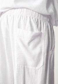 Hvide bomuldstrusser med elastisk linning og en enkelt påsyet lomme. Stoffet virker let med en let struktureret overflade.