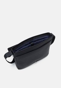 Borsa a spalla in pelle nera con superficie testurizzata, chiusura a zip, due scomparti interni e fodera in tessuto scuro. Cinghia regolabile inclusa.