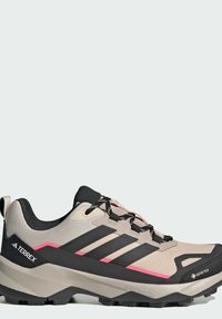 Μπεζ και μαύρο ορειβατικό παπούτσι Adidas Terrex με ροζ λεπτομέρειες, μαύρα κορδόνια, ετικέτα Gore-Tex και ανθεκτική σόλα για υπαίθριες δραστηριότητες.